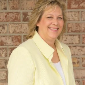 A CEO woman in a yellow jacket smiling in front of a brick wall.